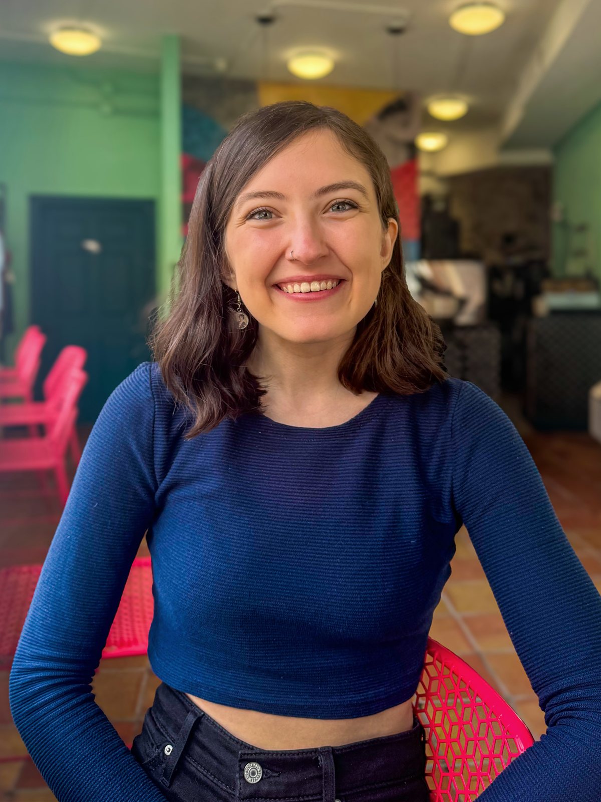 Bella, the creator of PHL Events, smiling in a colorful green and pink cafe